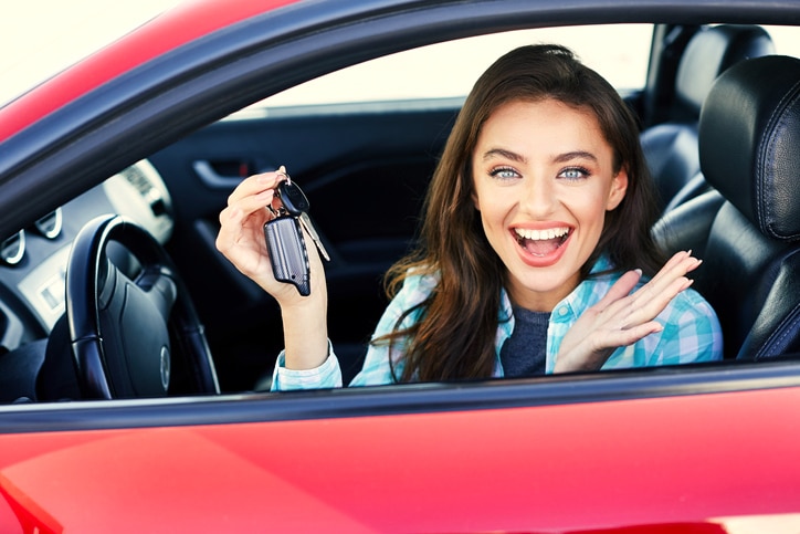 Woman behind the wheel of a red car excitedly holding car keys