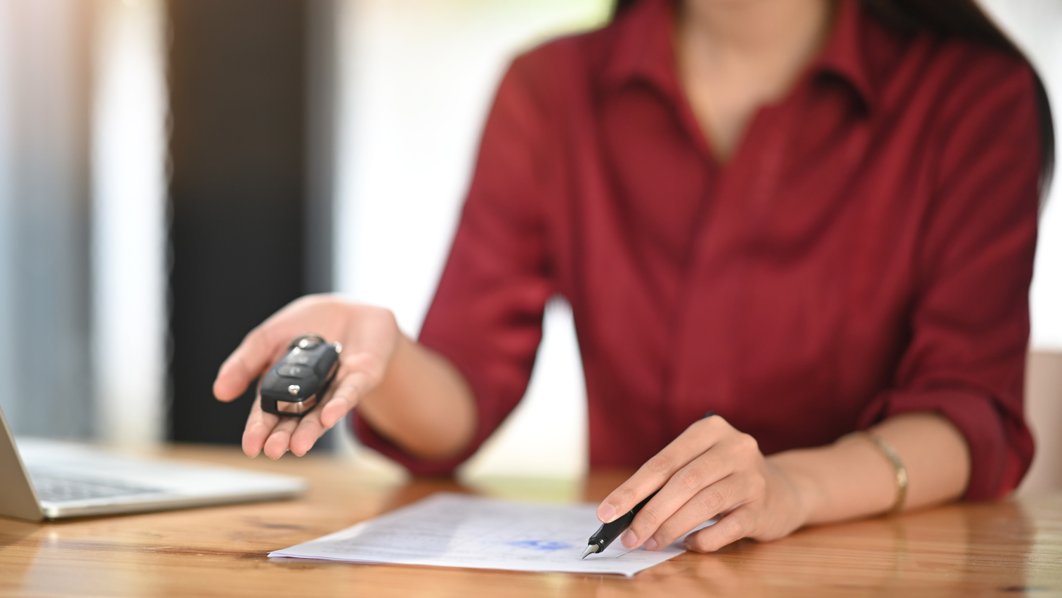 Employee showing customer where to sign contract while holding out the keys to a car